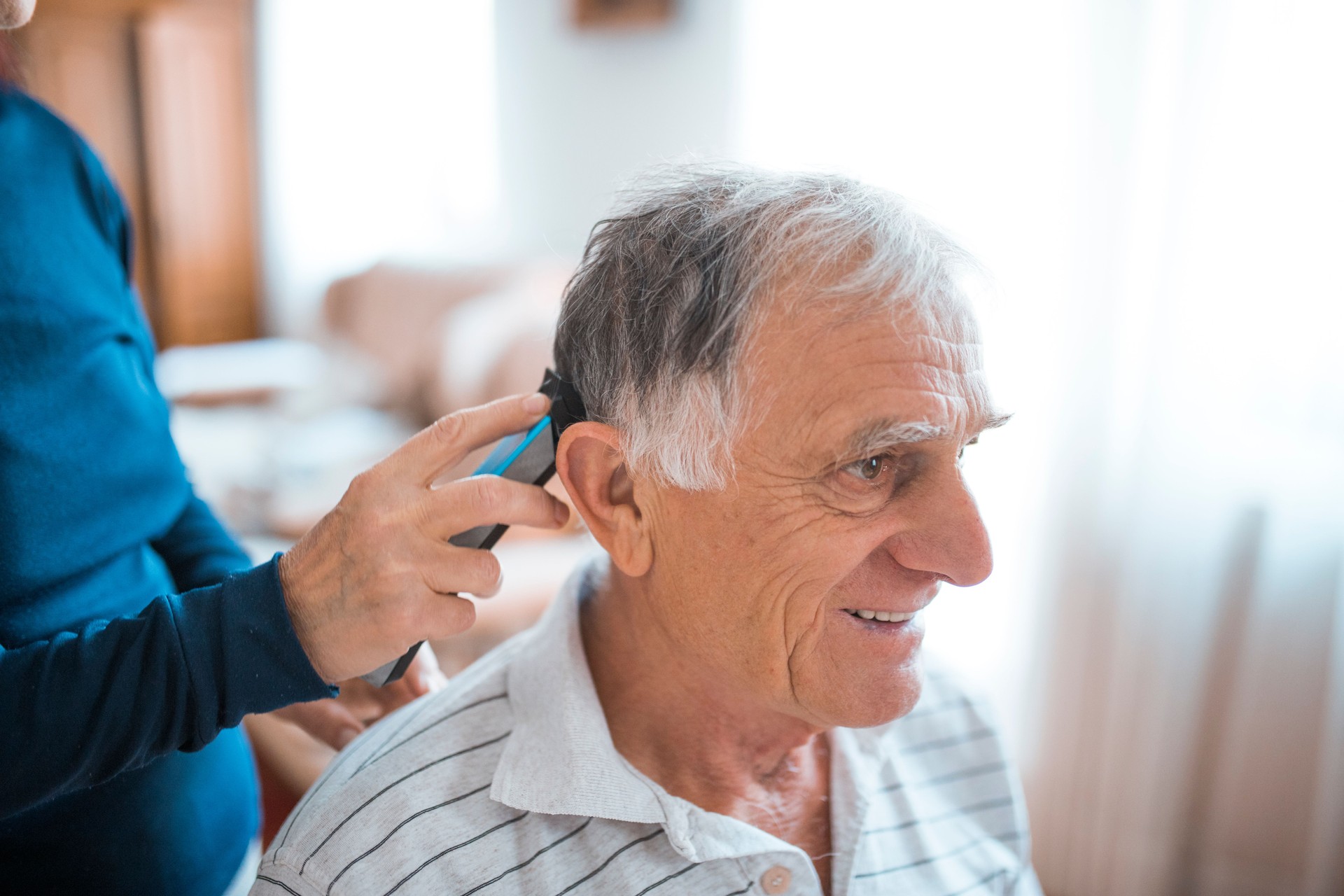 Woman cutting senior man's hair with electric razor at home during coronavirus quarantine