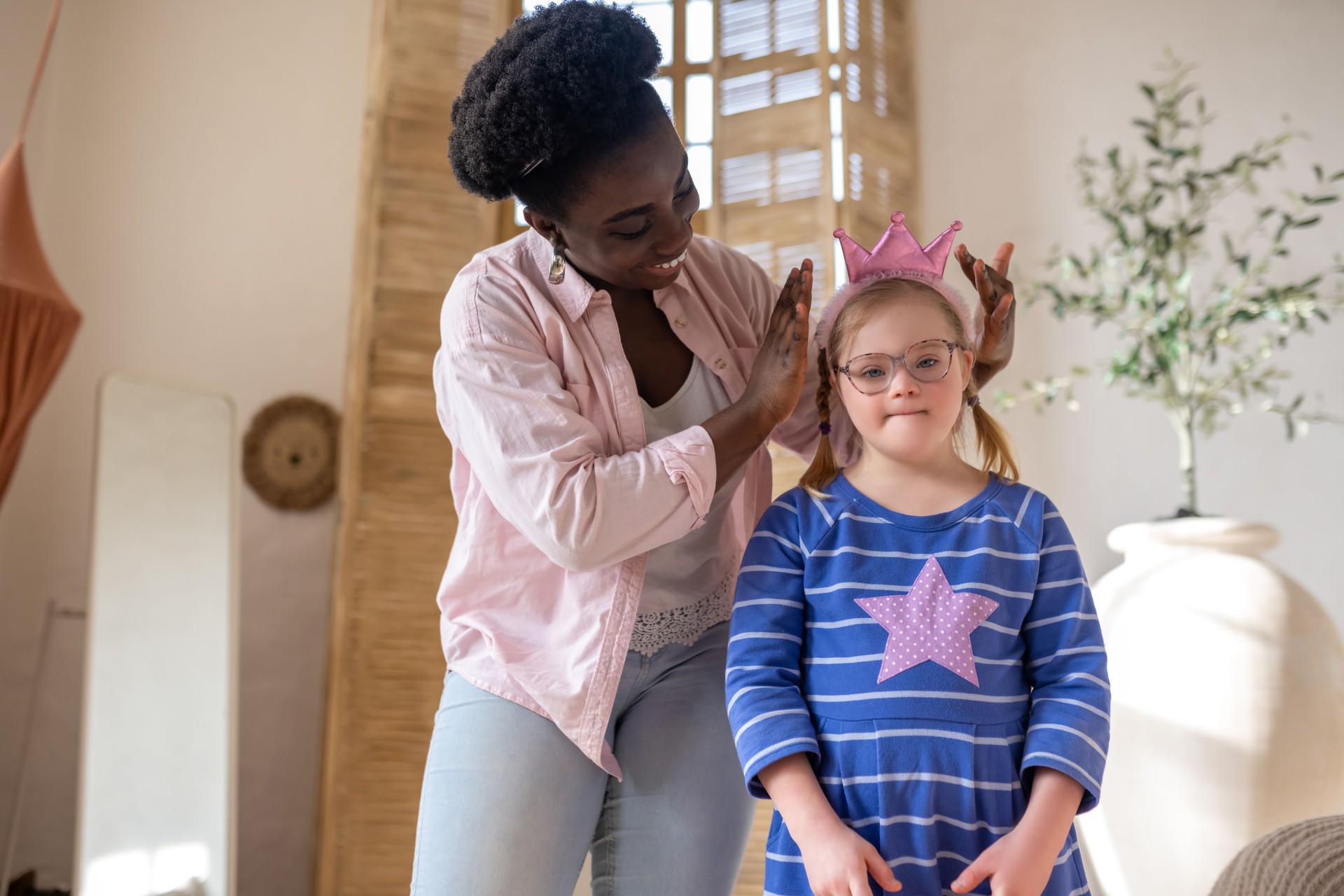 African american woman putting a crown on head of a girl in blue dress